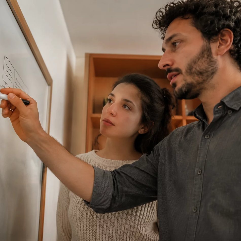 Duas participantes de pé junto ao quadro branco, desenhando as partes de um argumento